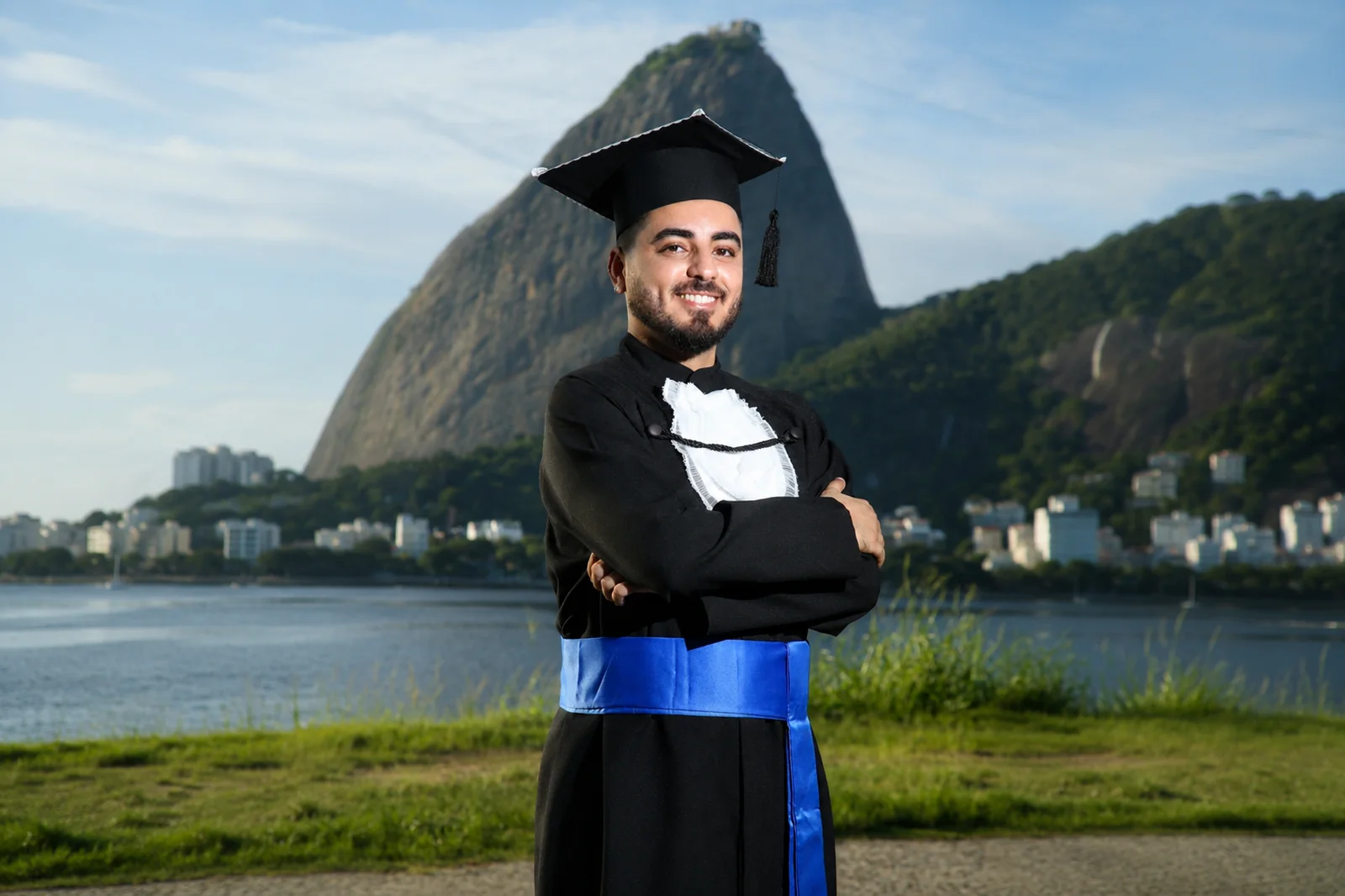 Psicólogo Douglas Almeida usando beca e capelo de formatura, com o Pão de Açúcar ao fundo, no Rio de Janeiro.